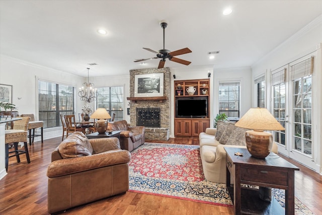 living room with crown molding, a fireplace, visible vents, wood finished floors, and ceiling fan with notable chandelier