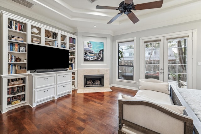 living room with dark wood-style flooring, a tray ceiling, crown molding, french doors, and a fireplace