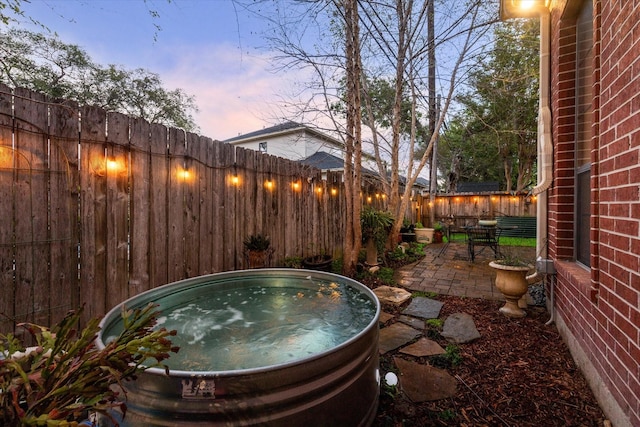 patio terrace at dusk featuring fence and a hot tub