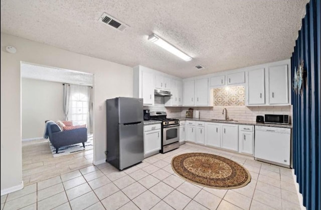 kitchen featuring sink, light tile patterned floors, appliances with stainless steel finishes, white cabinetry, and backsplash