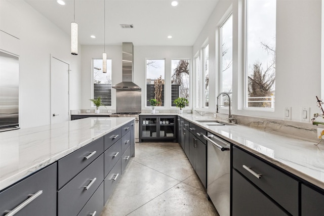 kitchen featuring appliances with stainless steel finishes, pendant lighting, sink, light stone countertops, and wall chimney exhaust hood