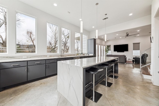 kitchen featuring a spacious island, a breakfast bar, light stone counters, decorative light fixtures, and ceiling fan