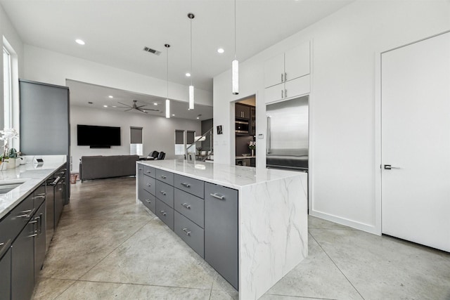 kitchen with gray cabinets, hanging light fixtures, a center island, light stone countertops, and white cabinets