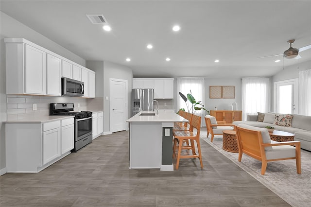 kitchen with stainless steel appliances, white cabinetry, a kitchen island with sink, and decorative backsplash