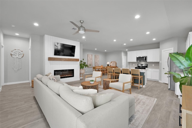 living room with ceiling fan, sink, a fireplace, and light hardwood / wood-style flooring