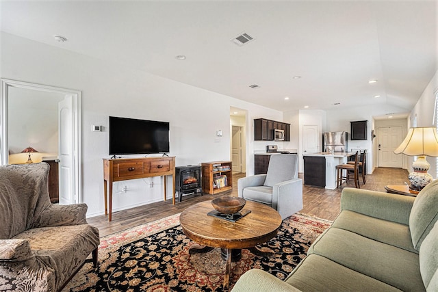 living room with vaulted ceiling, light hardwood / wood-style floors, and a wood stove