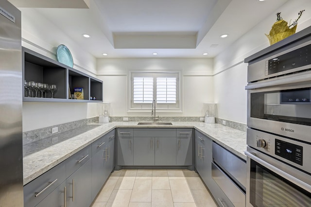 kitchen featuring sink, appliances with stainless steel finishes, gray cabinets, a raised ceiling, and light stone countertops