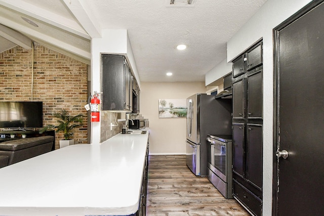 kitchen featuring vaulted ceiling with beams, light wood finished floors, light countertops, appliances with stainless steel finishes, and a textured ceiling