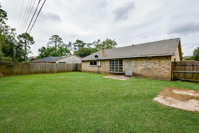 rear view of house with a fenced backyard, a lawn, a chimney, and brick siding