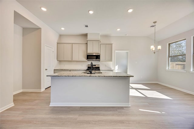 kitchen featuring a kitchen island with sink, light stone countertops, decorative light fixtures, and stainless steel appliances