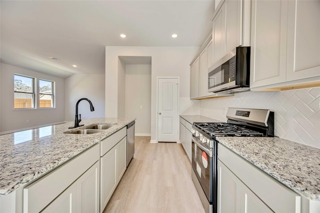 kitchen featuring sink, white cabinetry, stainless steel appliances, light stone counters, and a center island with sink