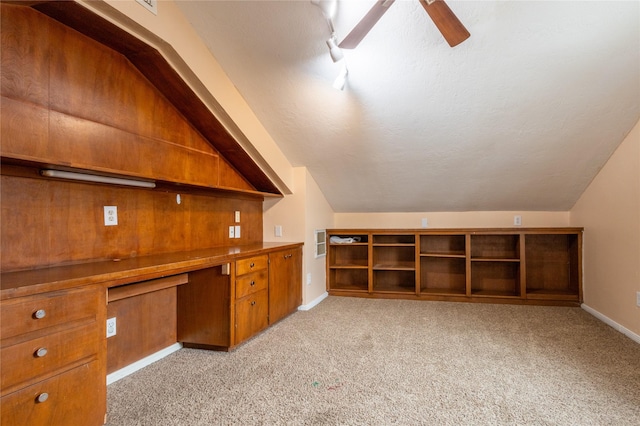 unfurnished office with vaulted ceiling, built in desk, light colored carpet, ceiling fan, and a textured ceiling