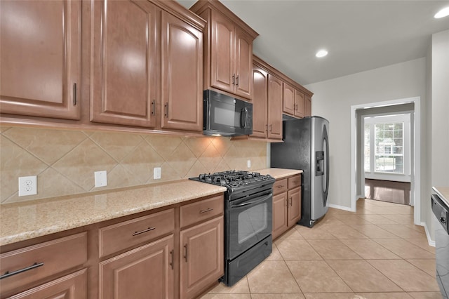 kitchen featuring light stone counters, backsplash, light tile patterned floors, and black appliances