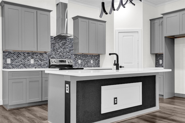 kitchen with wall chimney exhaust hood, crown molding, stainless steel electric range, a center island with sink, and gray cabinets