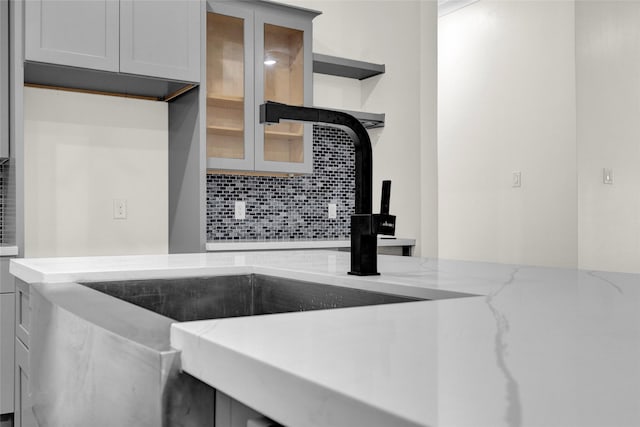 kitchen with gray cabinetry, light stone countertops, sink, and backsplash