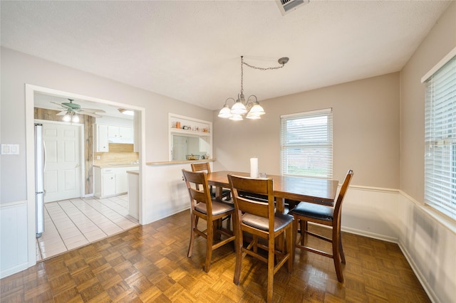 dining area with parquet floors, ceiling fan with notable chandelier, and a textured ceiling