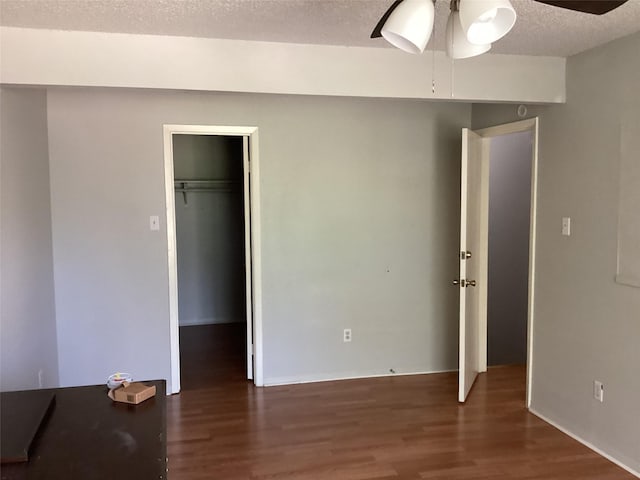 unfurnished bedroom with a walk in closet, a ceiling fan, a textured ceiling, wood finished floors, and a closet