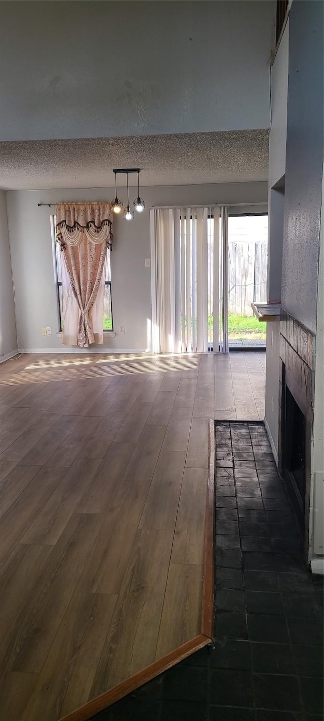 unfurnished living room with a tiled fireplace, dark wood finished floors, a textured ceiling, and baseboards