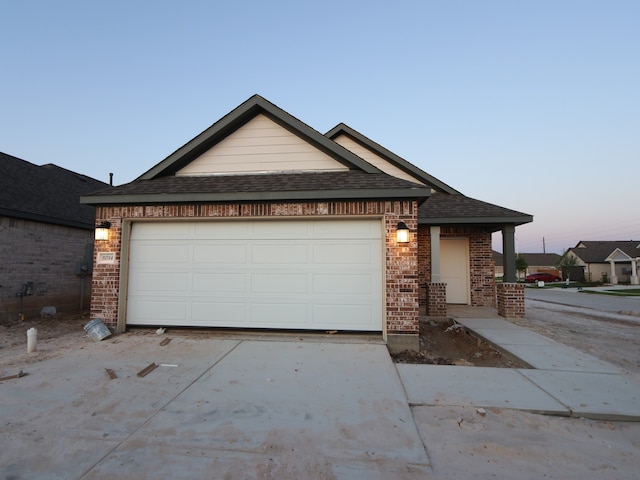view of front of home featuring driveway, brick siding, a shingled roof, and an attached garage
