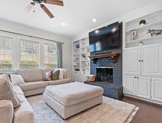 living room with dark wood-type flooring, built in features, ceiling fan, ornamental molding, and a brick fireplace