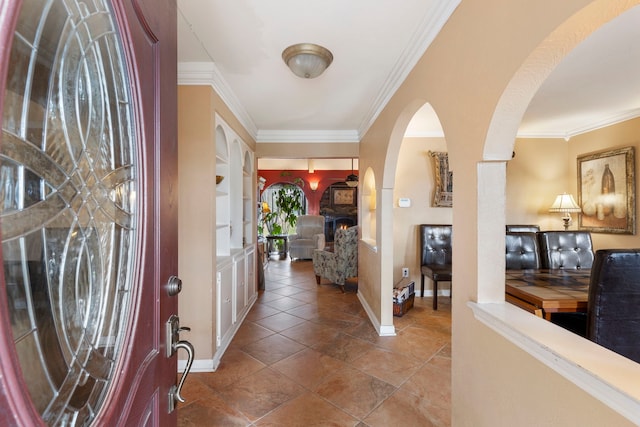 entrance foyer with tile patterned flooring, a lit fireplace, ornamental molding, and baseboards