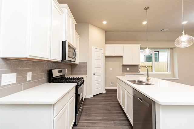 kitchen featuring decorative light fixtures, sink, white cabinets, stainless steel appliances, and a center island with sink