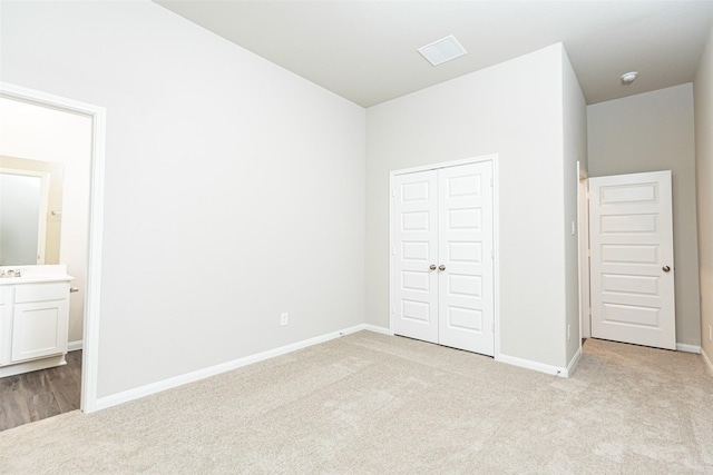 unfurnished bedroom with ensuite bathroom, light carpet, and a closet