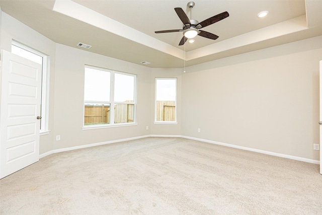 unfurnished room with ceiling fan, a tray ceiling, and light carpet