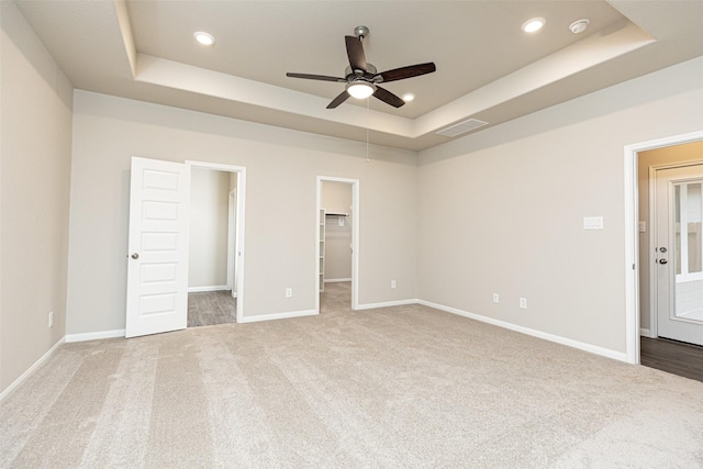 unfurnished bedroom featuring carpet flooring, a tray ceiling, ceiling fan, and a spacious closet