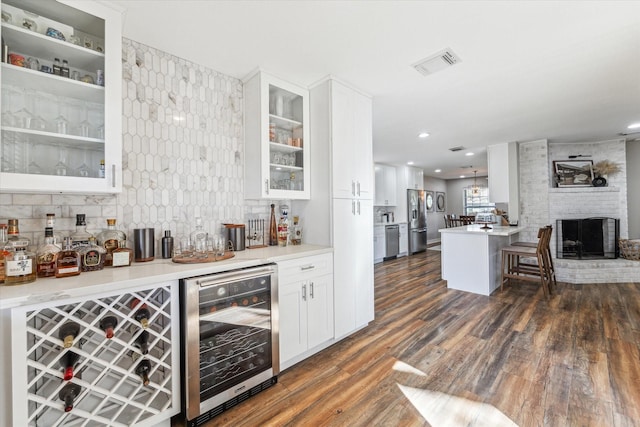 bar with beverage cooler, dark hardwood / wood-style floors, stainless steel appliances, a fireplace, and white cabinets