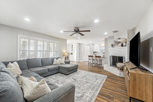 living room with dark wood-type flooring, ceiling fan, and a fireplace