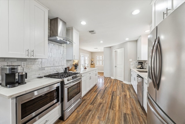 kitchen featuring wall chimney exhaust hood, white cabinetry, dark hardwood / wood-style floors, stainless steel appliances, and light stone countertops