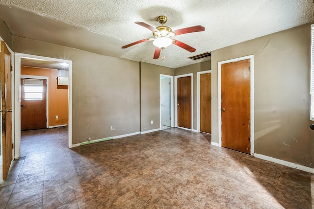 unfurnished bedroom featuring baseboards, visible vents, ceiling fan, a textured ceiling, and multiple closets