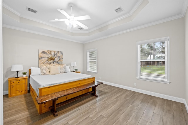 bedroom with ceiling fan, ornamental molding, a tray ceiling, and light hardwood / wood-style flooring