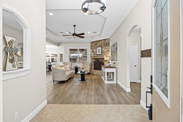 living room with light tile patterned floors, crown molding, ceiling fan, a tray ceiling, and a fireplace