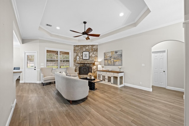 living room with crown molding, a fireplace, a raised ceiling, and light hardwood / wood-style flooring