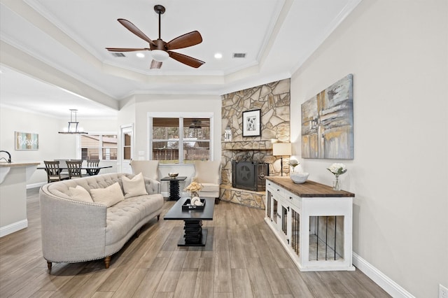 living room with ceiling fan, hardwood / wood-style floors, a tray ceiling, a fireplace, and ornamental molding