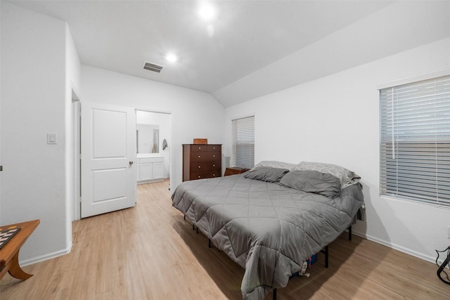 bedroom with ensuite bathroom, vaulted ceiling, and light wood-type flooring