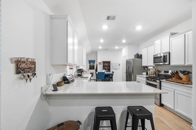 kitchen featuring a breakfast bar area, white cabinetry, light hardwood / wood-style flooring, appliances with stainless steel finishes, and kitchen peninsula