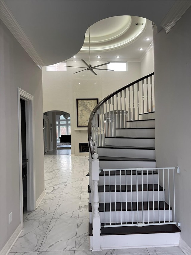 stairway with a tray ceiling, crown molding, ceiling fan, and a towering ceiling