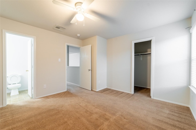 unfurnished bedroom featuring ceiling fan, ensuite bathroom, light carpet, a walk in closet, and a closet