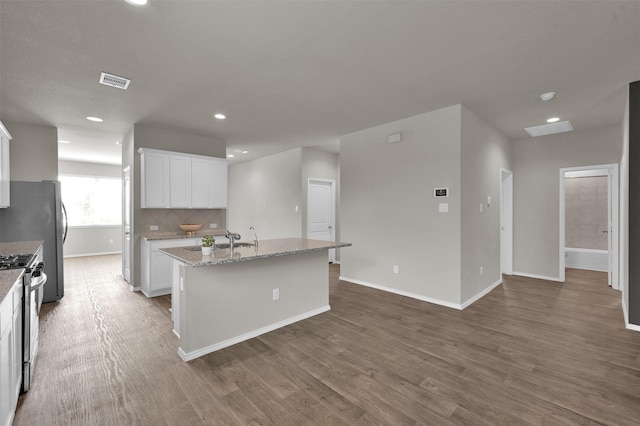 kitchen featuring light stone counters, an island with sink, hardwood / wood-style flooring, stainless steel appliances, and white cabinets