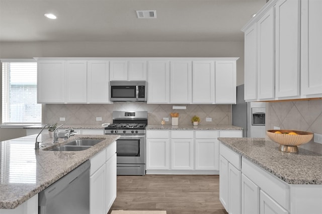 kitchen with sink, light hardwood / wood-style flooring, stainless steel appliances, tasteful backsplash, and white cabinets