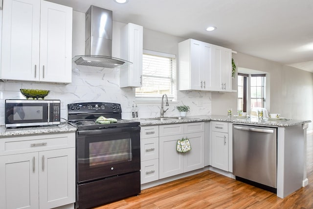 kitchen with wall chimney range hood, sink, light hardwood / wood-style flooring, appliances with stainless steel finishes, and white cabinetry