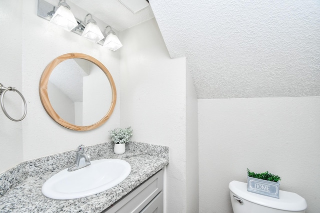 bathroom featuring vanity, vaulted ceiling, a textured ceiling, and toilet