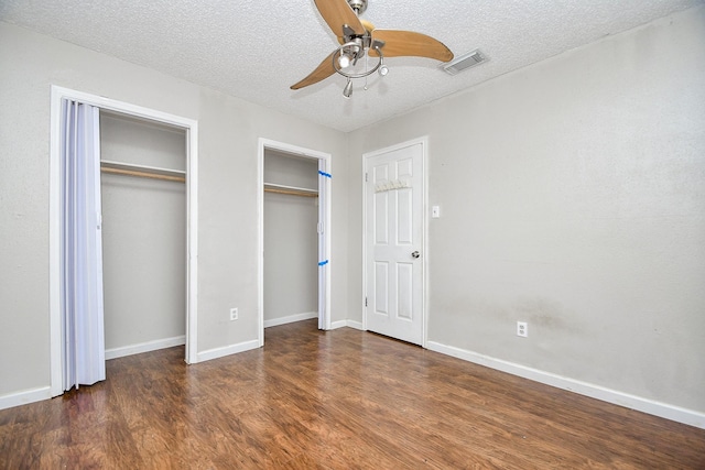 unfurnished bedroom with ceiling fan, two closets, dark wood-type flooring, and a textured ceiling