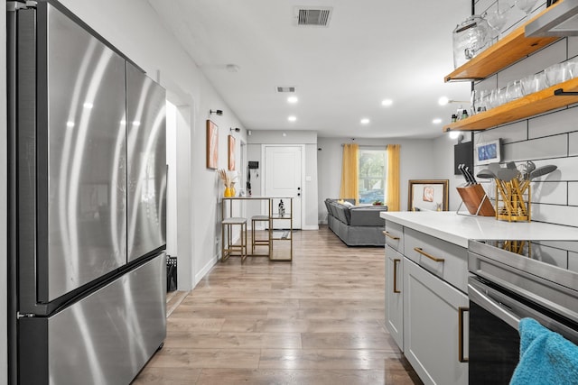 kitchen with appliances with stainless steel finishes, gray cabinets, and light hardwood / wood-style flooring