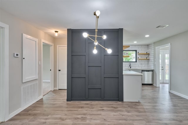 kitchen with tasteful backsplash, hanging light fixtures, dishwasher, and light wood-type flooring