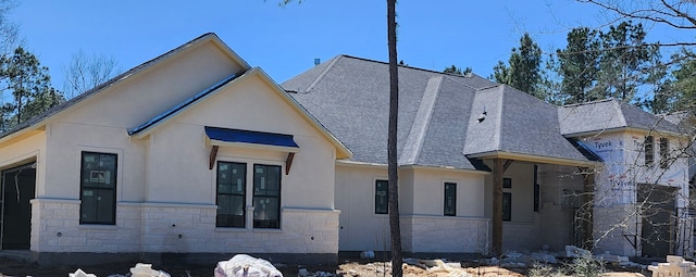 view of home's exterior with stone siding, roof with shingles, and stucco siding