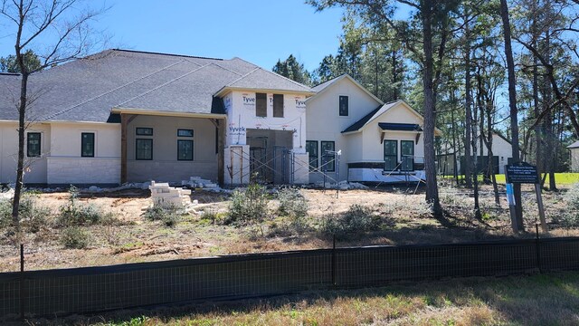 view of front facade with a shingled roof, fence, and stucco siding